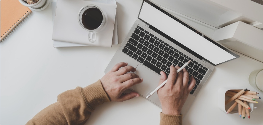 This is an image of a person typing on their laptop with a cup of coffee nearby.