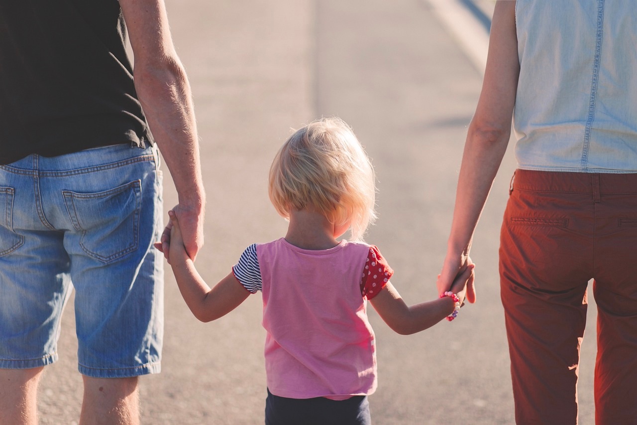 This is an image of a child holding both of their parents' hands.