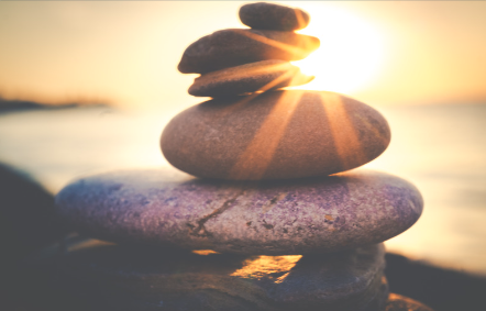 This is an image of rocks stacked up on a beach, with a sunset in the background.