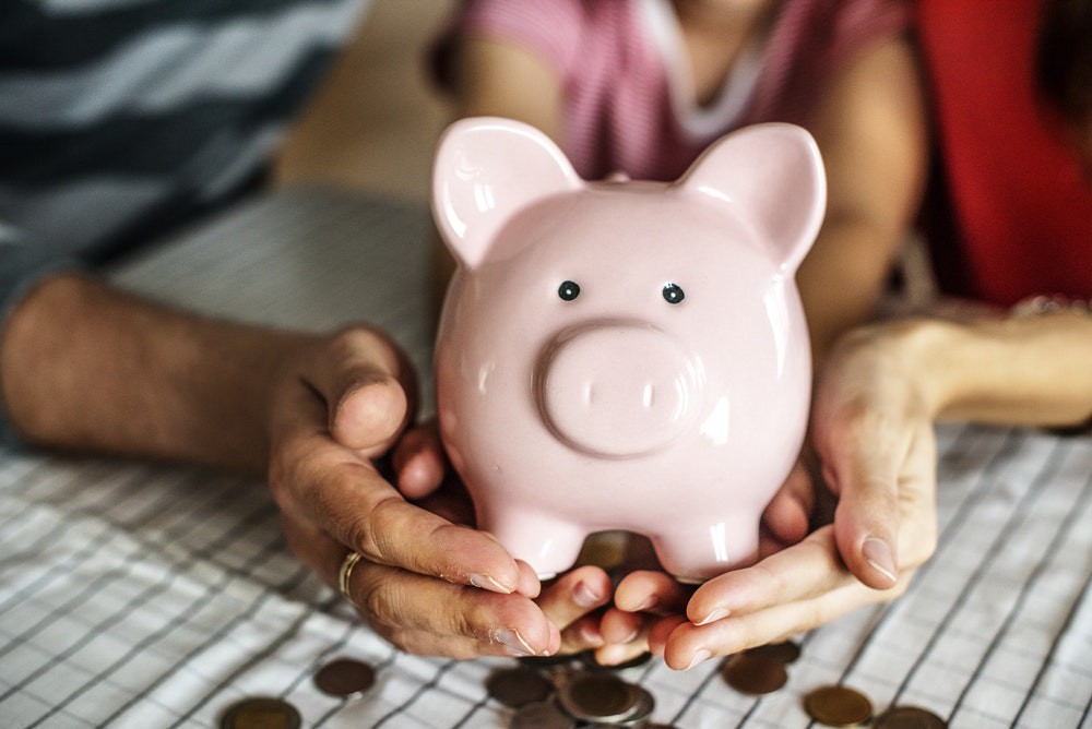 A husband, wife, and child holding out a piggy bank over coins