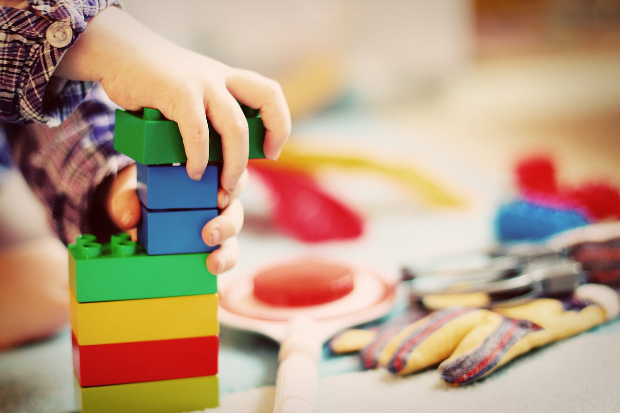 Picture of child’s hands building a tower using Lego-like blocks.