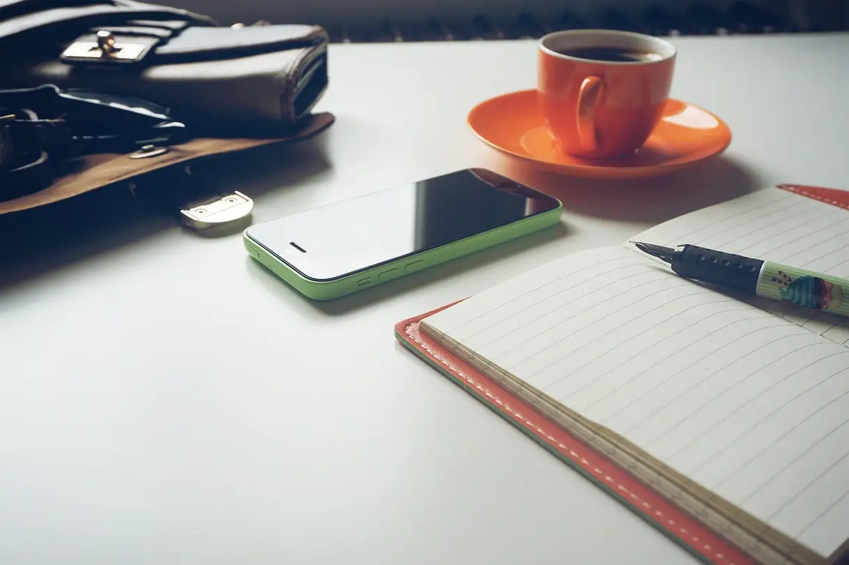 Calculating the Cost of Divorce This is a photo of a notebook, pen, phone, wallet, and cup of coffee.