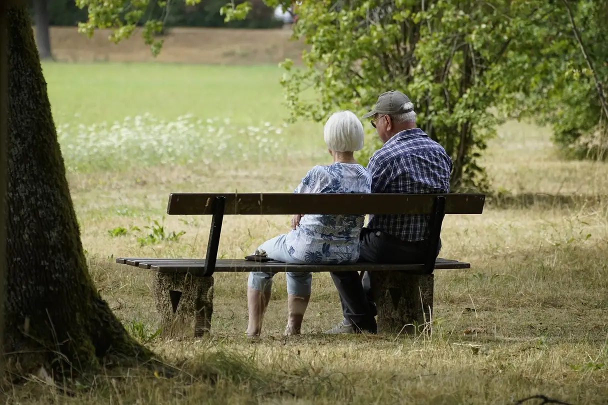 Spouses on a Bench This is an image of two elderly individuals sitting together on a bench outside.